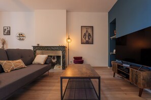Una sala de estar con sofá, mesa de centro, chimenea, mueble para televisor y una pared decorada con obras de arte.