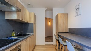 Une cuisine moderne avec des armoires en bois, un comptoir noir et un four encastré. On y trouve deux tabourets de bar et un luminaire fixé au mur.