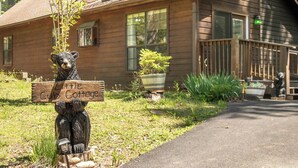 Une cabane en bois, ornée d’une statue d’ours tenant une pancarte, avec une véranda et un chemin menant à la maison.