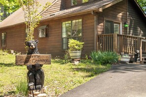 Eine Holzhütte mit einer Bärenstatue, die ein Schild hält, einer Veranda und einem Weg zum Haus.