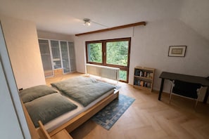 A bedroom with a bed, a window, a radiator, a bookshelf, and a desk.