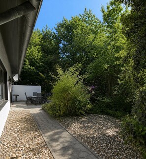 A patio area with a table and chairs, surrounded by trees and a gravel path.