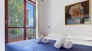 Un dormitorio con un ventanal grande, una cama con ropa de cama azul y un cuadro en la pared.