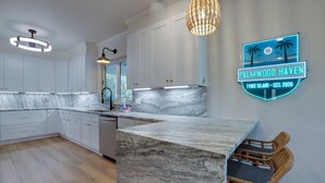 A modern kitchen with white cabinetry, a marble countertop, and a neon sign reading 'Palmwood Haven.' - Palmwood Haven | Private Pool, 2nd House From Sand! (Tybee Island)