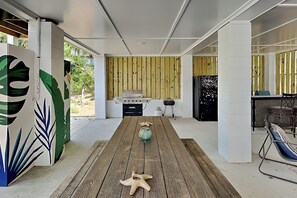 A modern kitchen with a wooden table, a grill, and a refrigerator. - Limetime Tybee | Vibrant, Upgraded, Outdoor Living (Tybee Island)