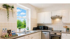Une cuisine moderne avec des meubles blancs, un lave-vaisselle, un four et une fenêtre donnant sur un paysage verdoyant.