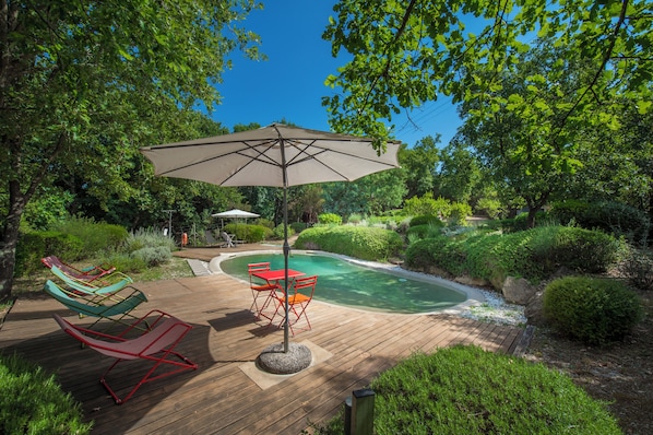 Une terrasse en bois avec une piscine, des chaises longues et un parasol.