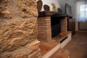 Une cheminée en pierre avec un manteau en briques, un téléviseur fixé au mur et une fenêtre avec des rideaux.