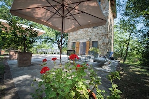 Un espace extérieur aménagé en patio, avec un bâtiment en pierre, un grand parasol et des plantes en pot.