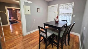 Un comedor con una mesa y sillas, una ventana con cortinas, y una puerta que conduce a otra habitación.