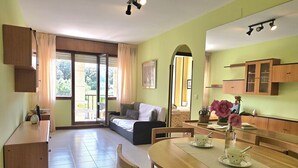 Una habitación con una mesa de comedor, sillas, un sofá, una zona de cocina y un ventanal corredero que da a un espacio exterior.
