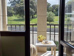 Un balcon avec une table, un panier de fleurs et une vue sur un parc.