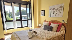 Un dormitorio con una cama, una mesita de noche, una lámpara, una ventana con cortinas y un cuadro en la pared.