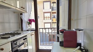Una cocina con estufa, horno y vistas a un balcón con un edificio al fondo.