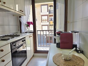 Eine Küche mit Herd, Backofen und Blick auf einen Balkon mit einem Gebäude im Hintergrund.