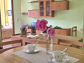 Ein Esstisch mit zwei Tassen und einem Blumenstrauß, Holzstühle und eine Küche mit Schränken im Hintergrund.