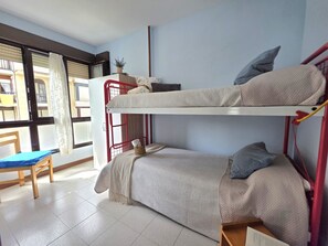 Une chambre de dortoir avec des lits superposés, une chaise, une fenêtre avec des rideaux et une petite table.