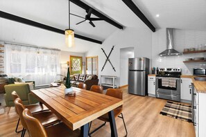 Eine moderne Küche mit Essbereich, ausgestattet mit einem Holztisch, Stühlen, einem Deckenventilator und einem Edelstahl-Kühlschrank.