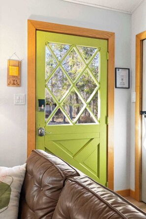 Eine grüne Tür mit einem diamantenmusterten Fenster, ein braunes Ledersofa und ein gerahmtes Zertifikat an der Wand.