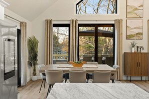 Un espace repas moderne avec une grande table, des chaises, une plante en pot et une vue dégagée grâce à de grandes fenêtres.