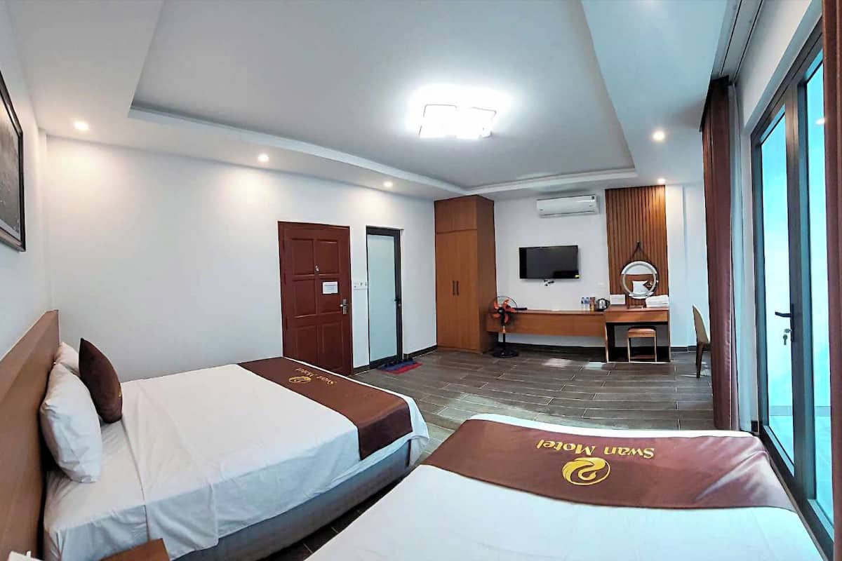 Una habitació d'hotel amb dos llits, una taula de treball, una televisió i una finestra gran.