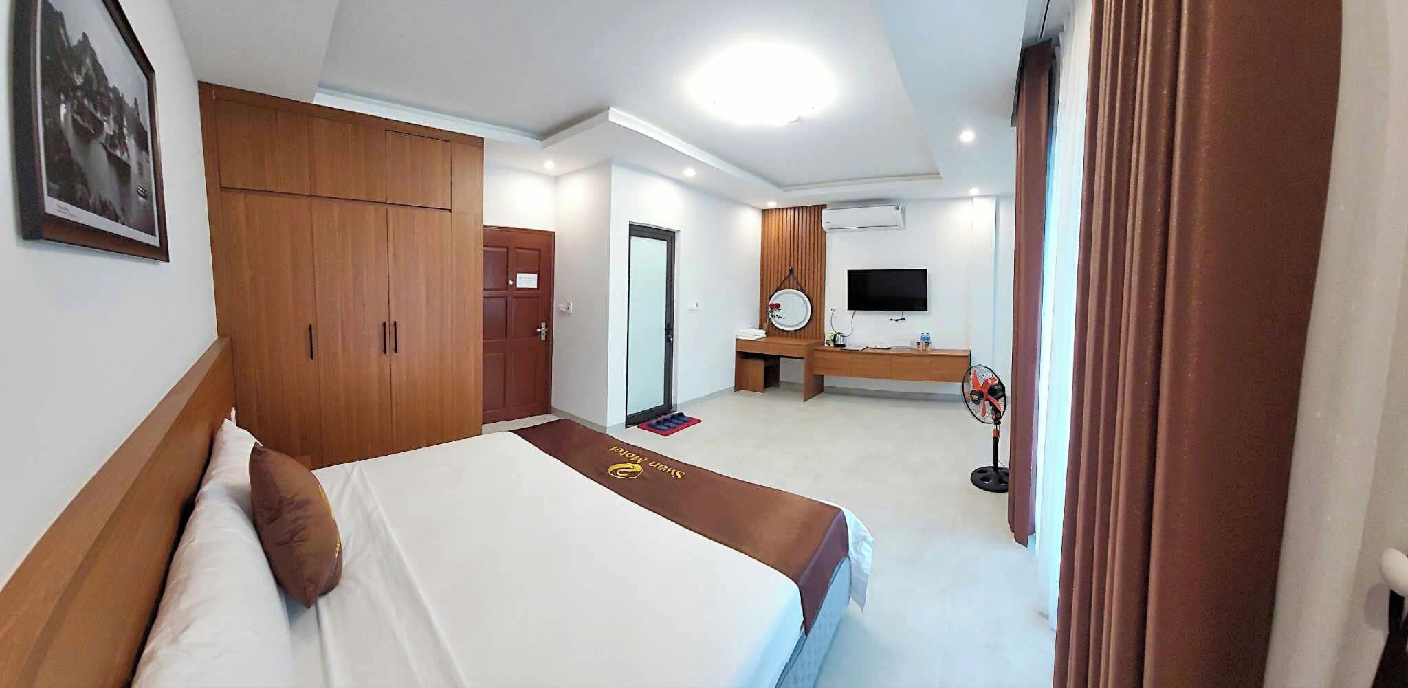 A hotel room with a bed, wardrobe, desk, and a television.