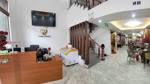 Eine Hotelhalle mit Empfangsschalter, einer Treppe und einem Essbereich mit Tischen und Stühlen.