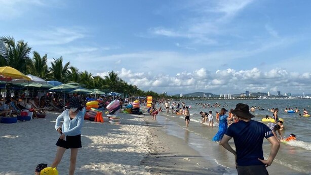 Ein Strand mit Sonnenschirmen, Menschen und Wassersport.