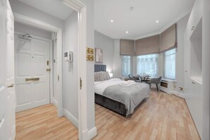 A bedroom with a bed, bedside table, chair, and a window with a view. - Cosy & Bright Studio in Knightsbridge (Greater London)