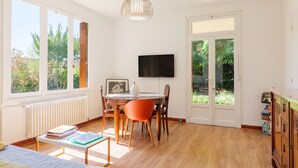 Una habitación con una mesa de comedor, sillas, televisor y ventanas amplias.