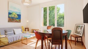 Una habitación con sofá, mesa de comedor, sillas, lámpara colgante y ventana con vista a follaje.