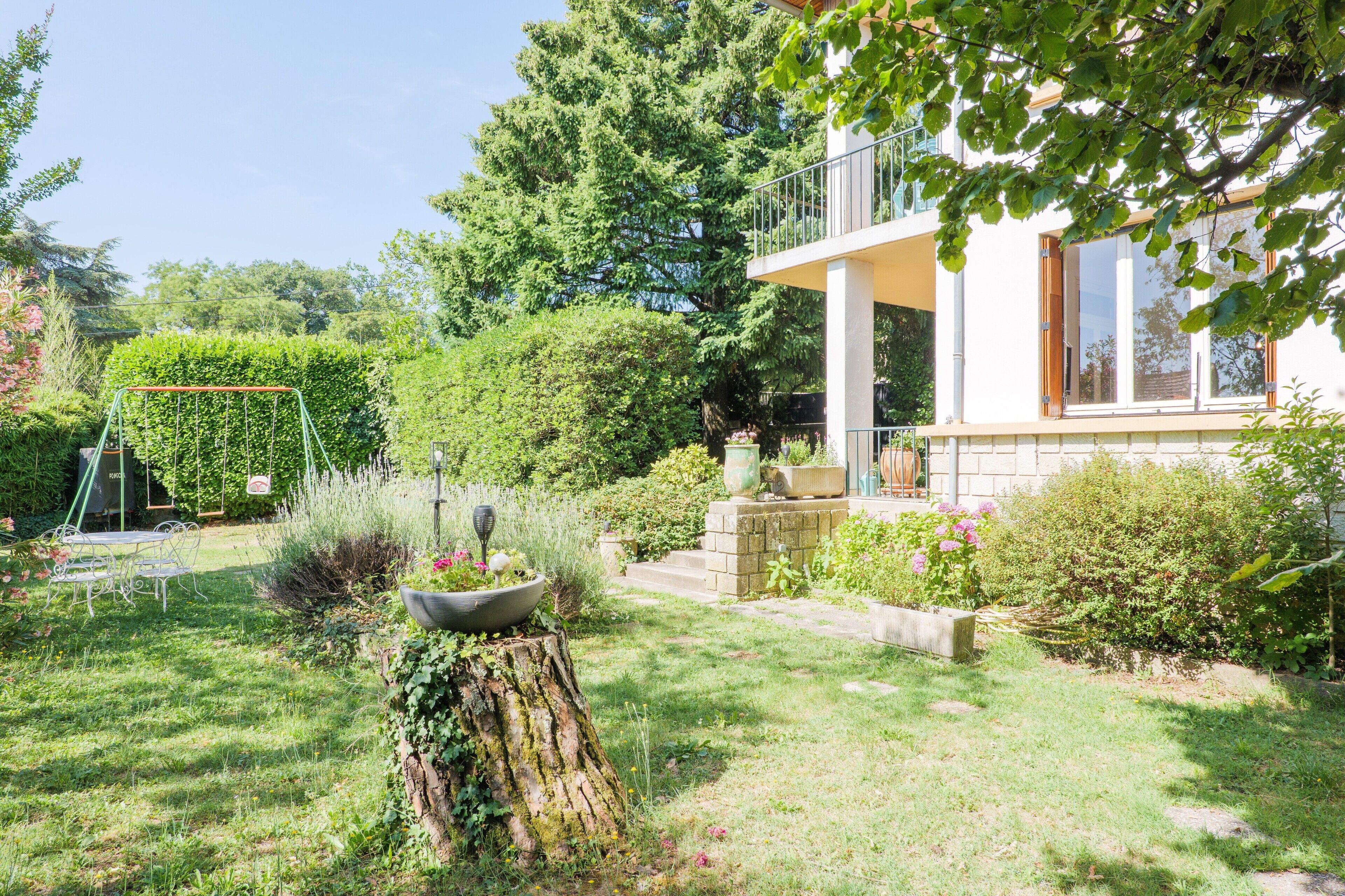 Ein Garten mit Schaukel, Baumstumpf und einem Haus mit Balkon.