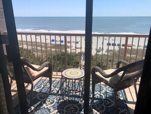 Un balcon avec vue sur la plage, deux fauteuils en osier, une petite table ronde et un sol à motifs.