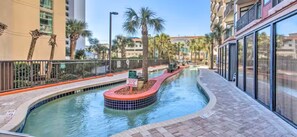 A swimming pool with a curved design, surrounded by palm trees and a brick walkway. - Oceanfront Couple’s Hideaway on the “Golden Mile” (Myrtle Beach)
