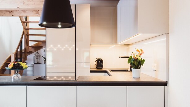 A modern kitchen with a black pendant light, a fruit bowl on the counter, and a potted plant. - Klochberg R&L APP Sunrise - Gelber Muskateller (Kloech)
