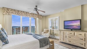 A bedroom with a large bed, a ceiling fan, a TV, a chair, and a view of the ocean. - Two-Story penthouse with stunning Gulf views (Miramar Beach)