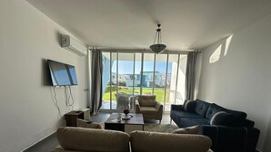 Ein Wohnzimmer mit einer Couch, einem Couchtisch, einem Fernseher und Blick auf einen Balkon mit Gartenmöbeln.
