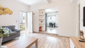 Uma sala de estar moderna com um sofá, uma mesa de centro e uma área de jantar ao fundo.