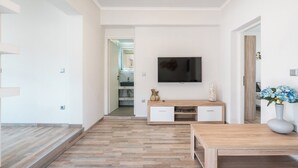 Uma sala de estar moderna com piso de madeira, televisão fixada na parede, mesa de centro de madeira e um vaso com flores.