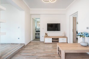 Ein modernes Wohnzimmer mit Holzboden, einem an der Wand montierten Fernseher, einem Couchtisch aus Holz und einer Vase mit Blumen.