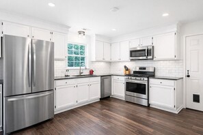 A modern kitchen with white cabinetry, stainless steel appliances, and a wooden floor.