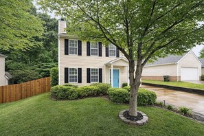 A two-story house with a front porch, a blue door, and a tree in the front yard.