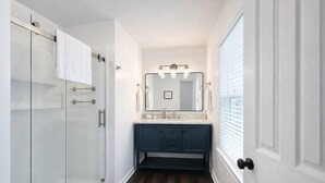 A bathroom with a glass shower enclosure, a dark blue vanity, and a white door.