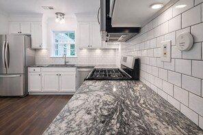 A modern kitchen with white cabinetry, a granite countertop, a stainless steel refrigerator, and a built-in stove.