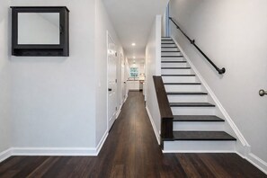 A hallway with a staircase, white walls, and dark wooden flooring.