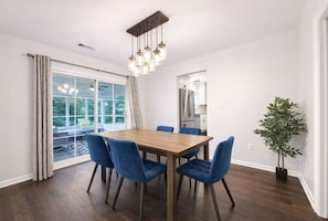 A dining area with a wooden table and blue chairs, a potted plant, and a view through a large window.