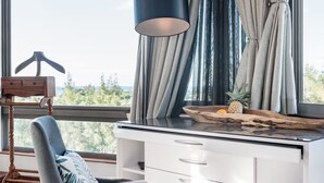 Een moderne kamer met een bureau, stoel en grote ramen voorzien van gordijnen.