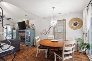 A dining area with a round wooden table, white chairs, a blue cabinet, a television, and a decorative wall piece. - Quiet 4BR Retreat Prefect for Families and Groups (Spartanburg)