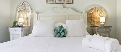 A neatly made bed with white linens, a decorative mirror, and a wall sign that reads 'home sweet home.'
