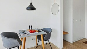 Zona pranzo moderna con tavolo, due sedie, lampada a sospensione, specchio a parete e una porta.